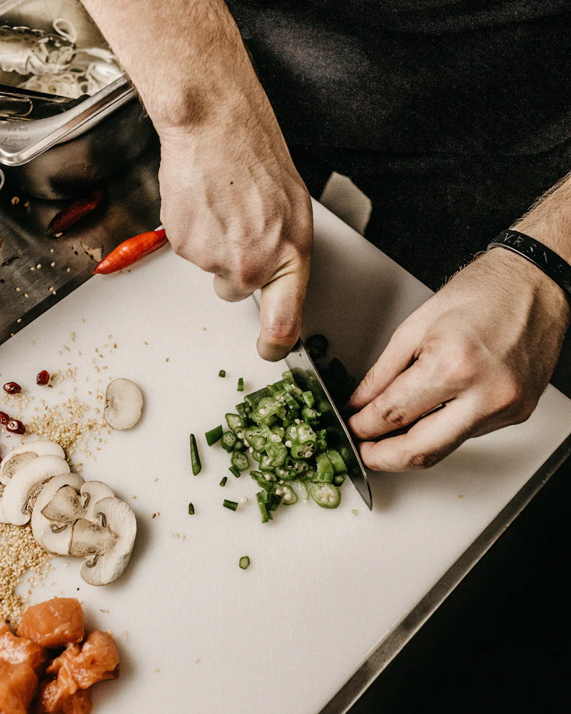 Mains du chef ciselant les légumes du marché sur la planche