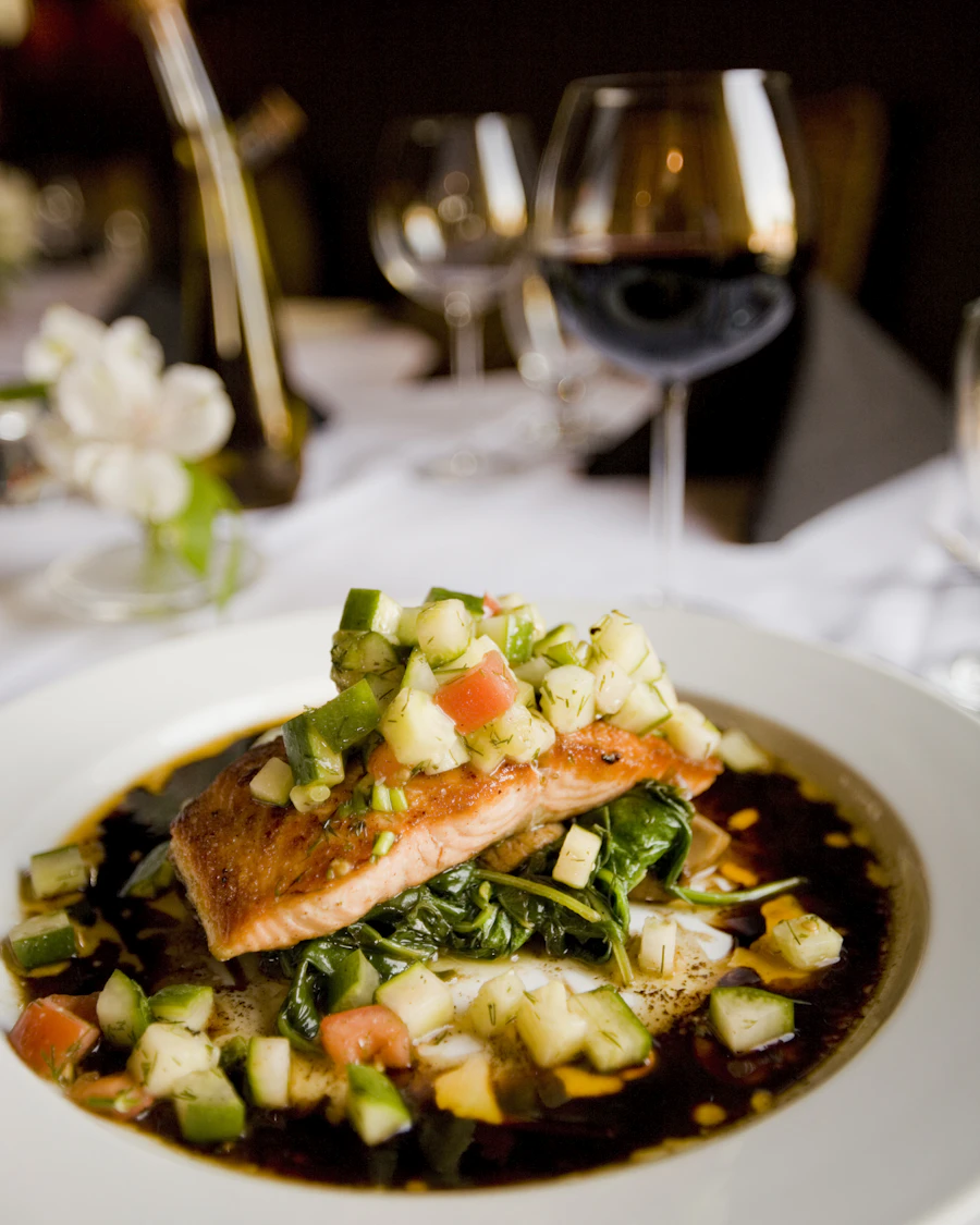 Plat signature dressé à l'assiette, verre de vin en arrière-plan